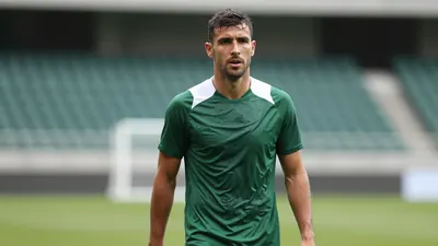 Mid-30s muscular player, waist-up, dark green and white plain training top, sweat-damp fabric clinging to torso, focused...