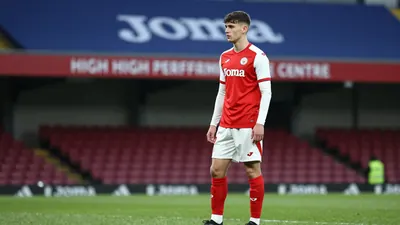 A young, anonymous Swansea City U21s player in a red jersey with white sleeves, wearing a white pair of shorts with a red...