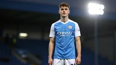 A 19-year-old centre-back in Swansea City's Under-21s kit, with a confident expression, standing in front of a blurred...