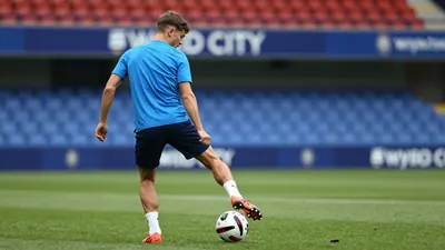 A 26-year-old attacking midfielder, dressed in Swansea City's blue kit, with his back to the camera, looking focused as...