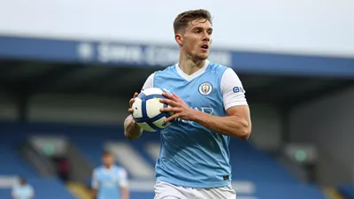 A tight waist-up shot of a Swansea City player in a blue jersey with white sleeves, holding a football and looking...