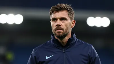 A mid-30s male coach in a navy blue Swansea City training jacket, head-and-shoulders, focused expression, background...