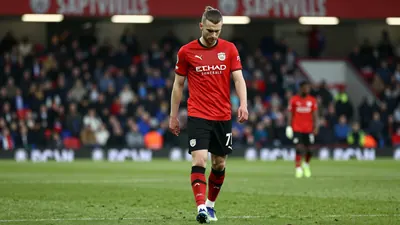 A tight waist-up shot of an anonymous Swansea City player in a red jersey and black shorts, looking dejected as he walks...