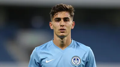 A young male footballer, mid-20s, athletic build, wearing a solid sky-blue kit, head-and-shoulders shot with a shallow...